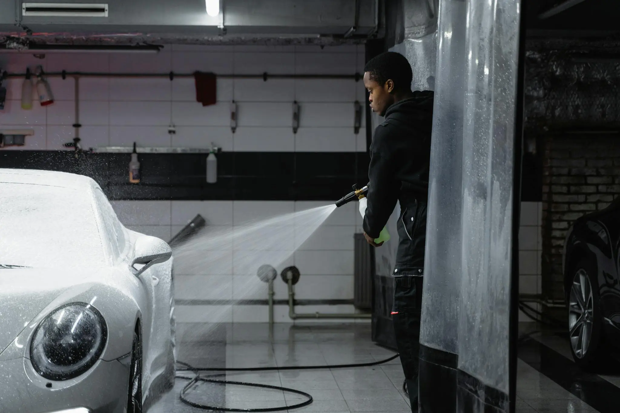 A person using a pressure washer to clean a car in an indoor garage setting.